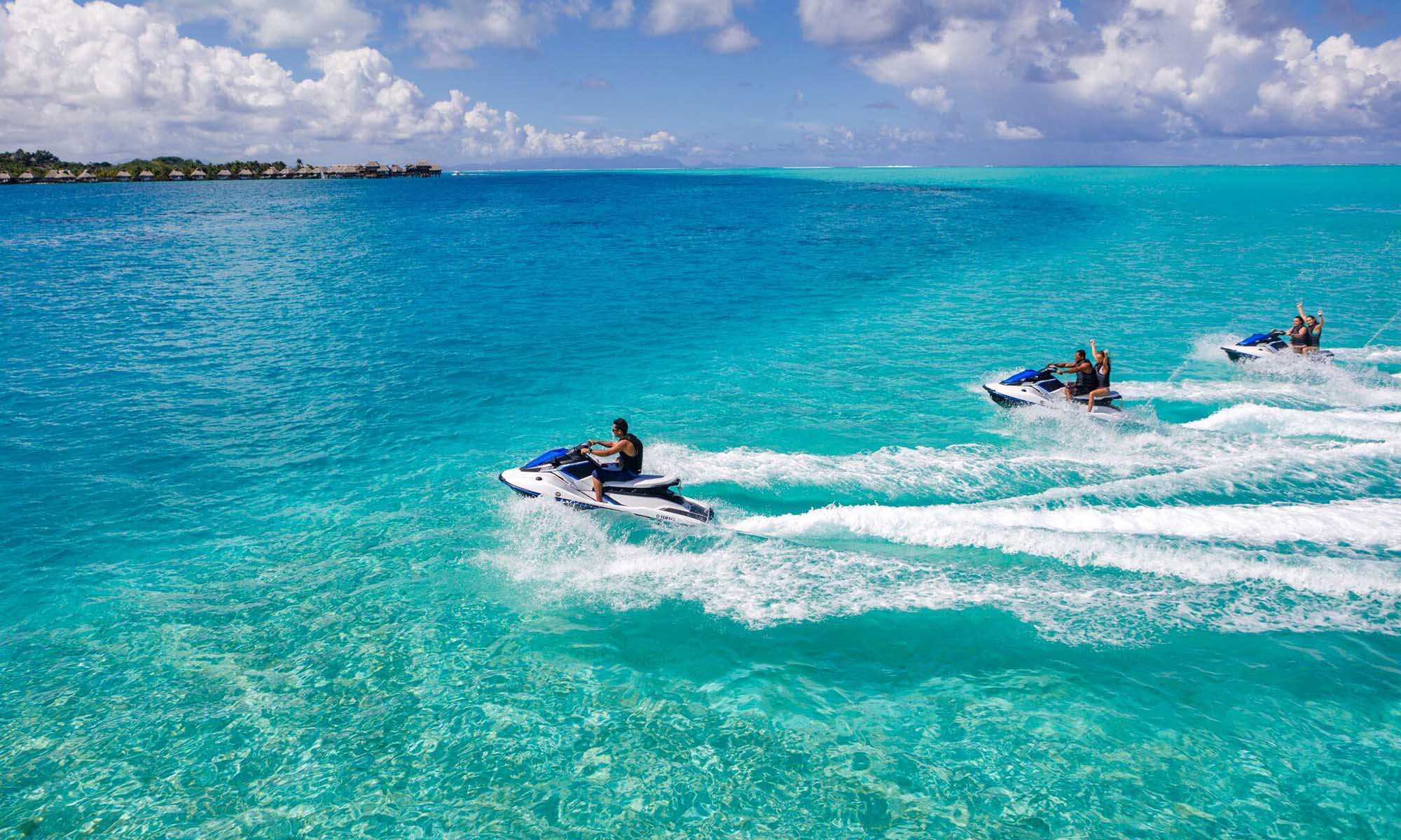 Guests riding jet skis across a clear turquoise lagoon